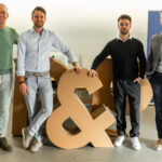 Directieteam van Wings Group en P&P Company bij fusie, staand naast groot &-symbool tijdens aankondiging samenwerking