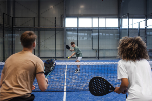Drie mensen spelen een padelwedstrijd op een indoor padelbaan in Limburg.